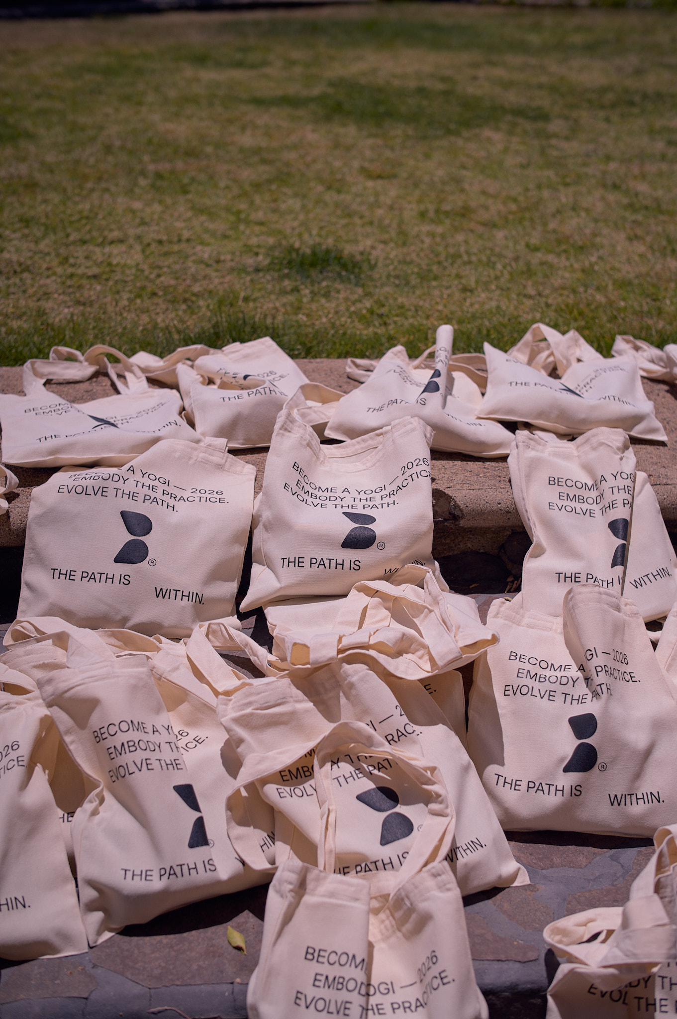 Become A Yogi 2026 cotton tote bags arranged on stone steps, printed with the mantra Embody the Practice. Evolve the Path. The Path is Within.
