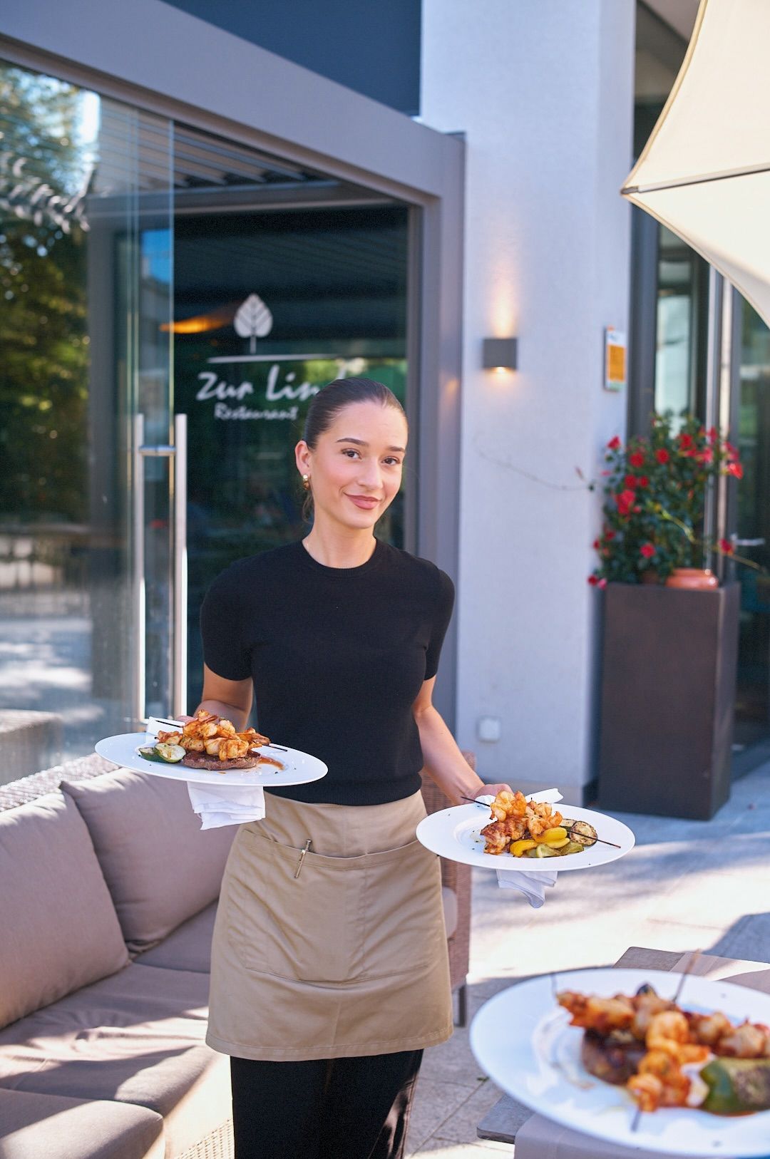 A server crossing the terrace with plates in hand, front of house at Zur Linde.
