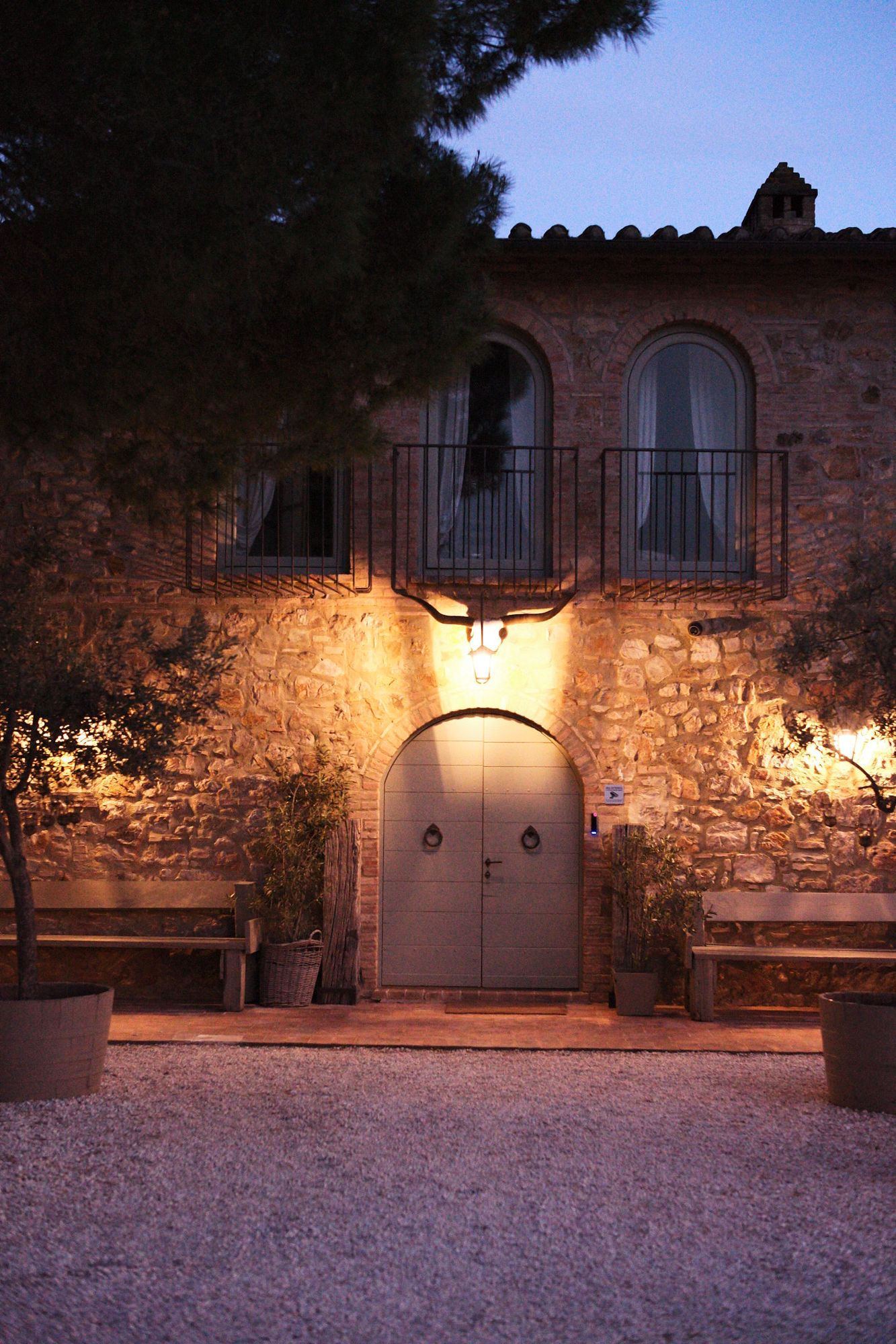 A Tuscan stone villa glowing under warm light at dusk, cypress trees nearby.